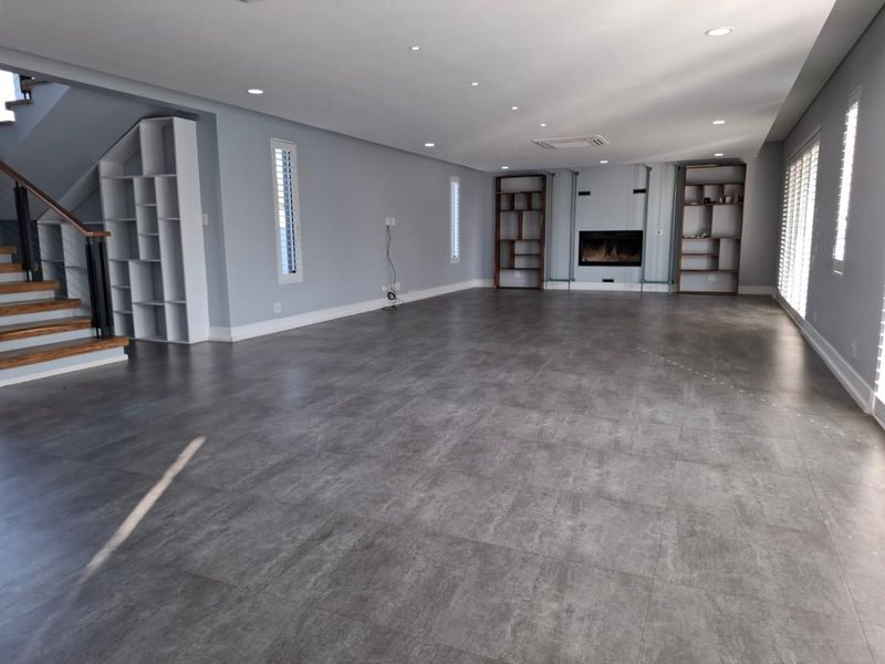 Spacious open-plan living area featuring large format floor tiles, a built-in fireplace, integrated shelving, and a modern staircase with wooden treads.
