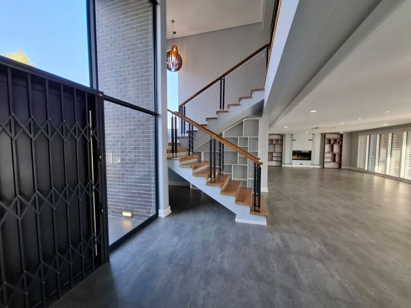 Spacious entrance hall featuring a modern timber staircase, built-in shelving, and a sleek fireplace, leading into an expansive open-plan living area.