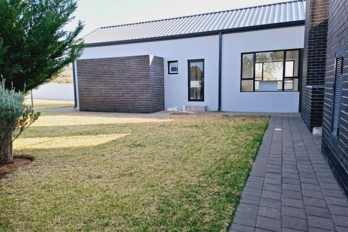 A well-maintained rear exterior view featuring a modern brick and plaster facade, metal roofing, and a paved walkway leading through the garden.