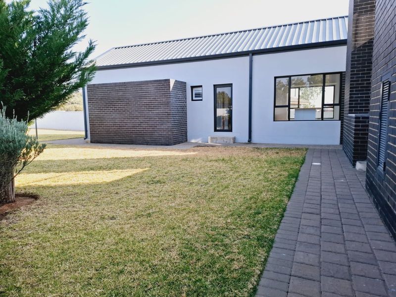 A well-maintained rear exterior view featuring a modern brick and plaster facade, metal roofing, and a paved walkway leading through the garden.