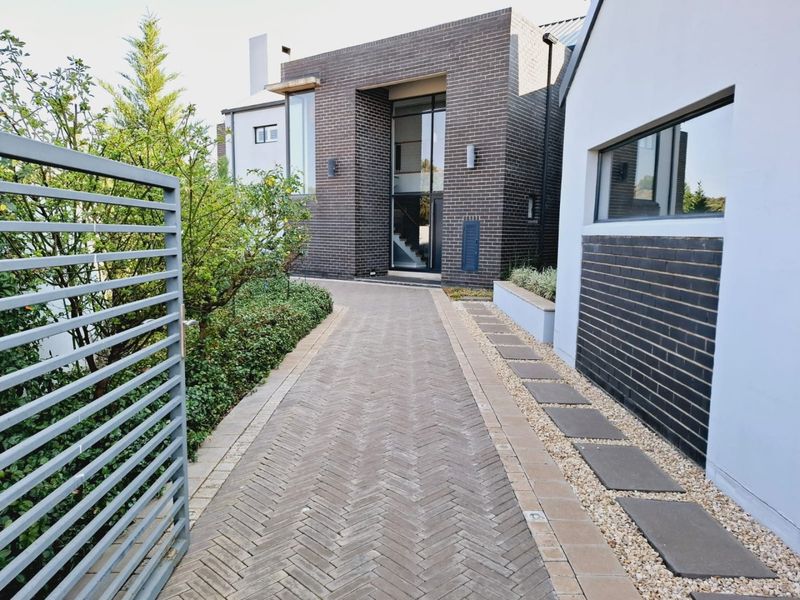 A modern front entrance featuring a herringbone brick driveway, metal gate, and contemporary brick and rendered facade with landscaped stone pathways.