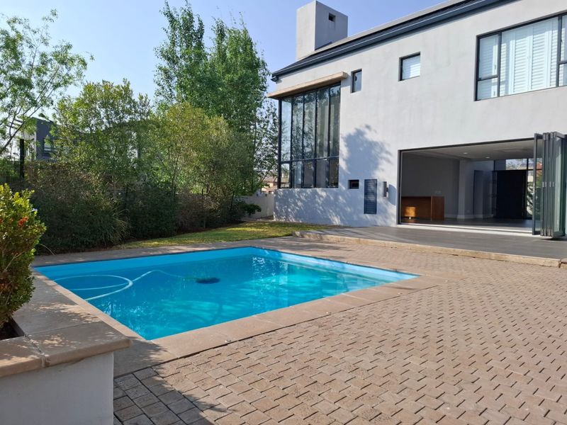 A modern rear exterior view featuring a swimming pool, paved patio area, and large bi-fold doors leading into the main living space.