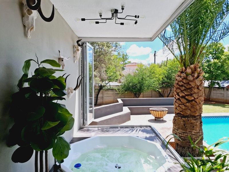 Covered patio area featuring a built-in jacuzzi, bi-fold doors opening to a paved outdoor space with built-in seating and a swimming pool.