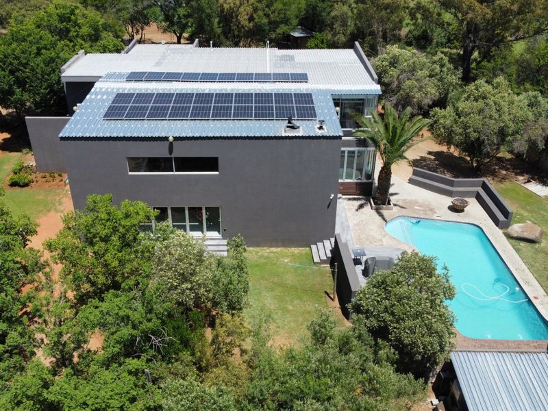 Aerial view of a modern house featuring a large swimming pool, landscaped garden, and extensive solar panel installation on the roof.