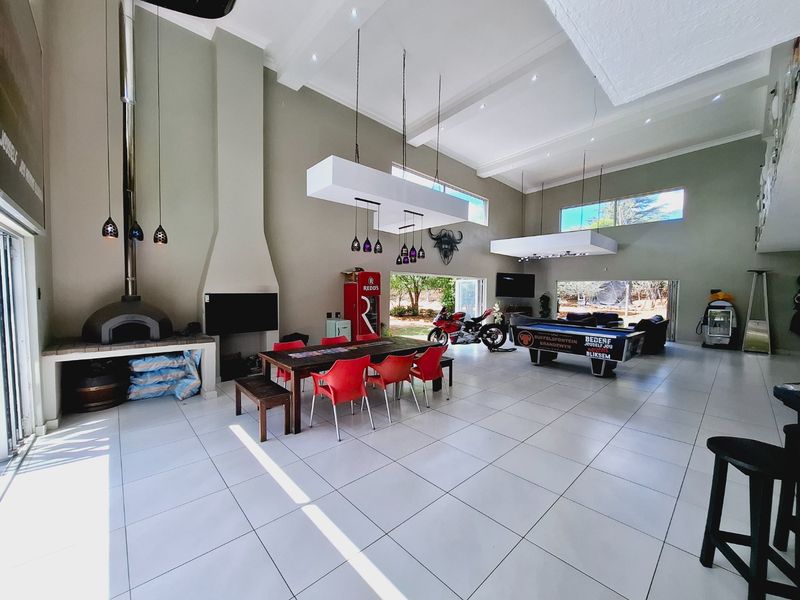Spacious open-plan living and dining area featuring high ceilings, tiled floors, a built-in fireplace, and a pizza oven with seamless access to the outdoors.