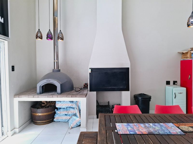 Covered patio area featuring a built-in pizza oven and a fireplace, finished with tiled flooring and modern pendant lighting.