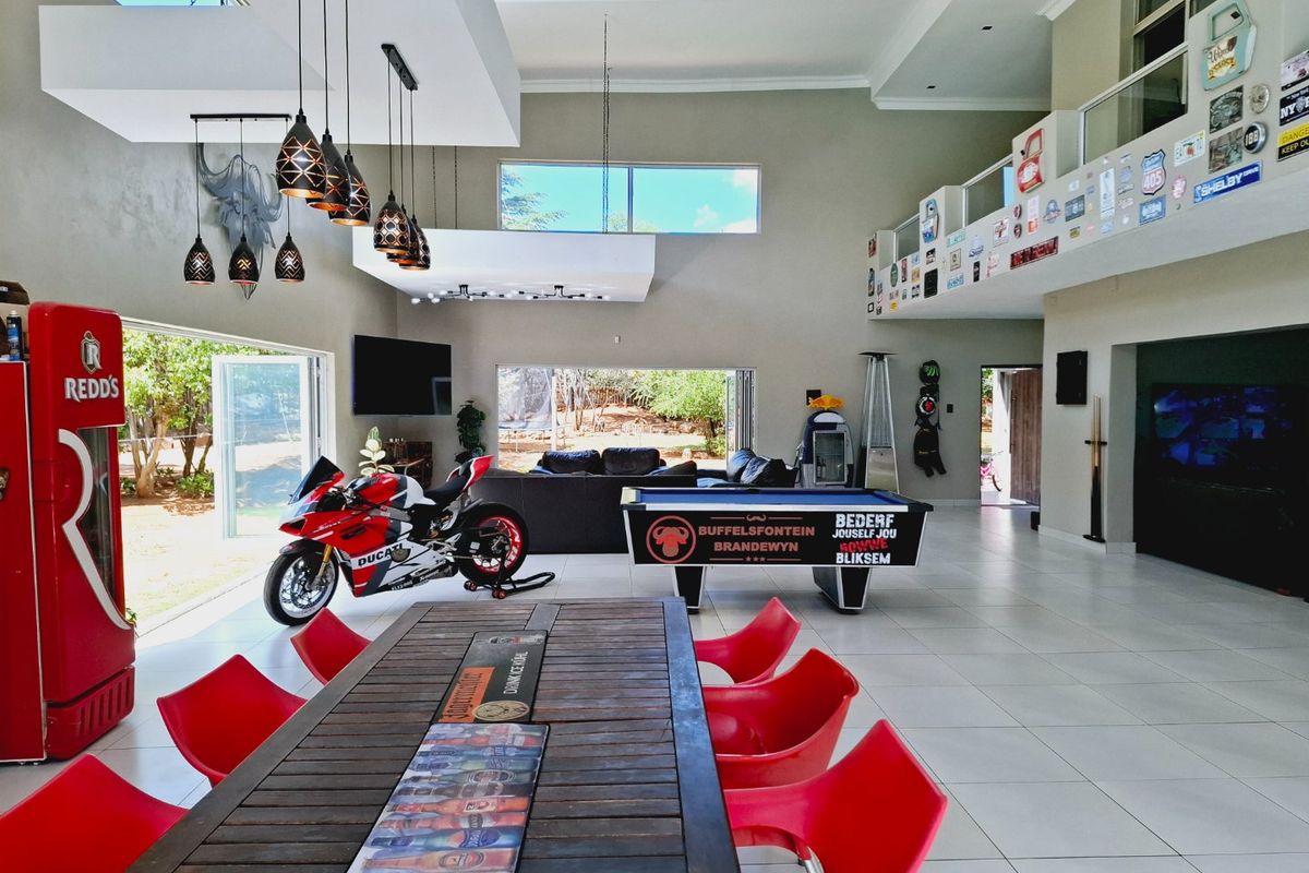 Spacious open-plan living area featuring high ceilings, tiled flooring, large bi-fold doors opening to the garden, and a mezzanine level with glass balustrades.