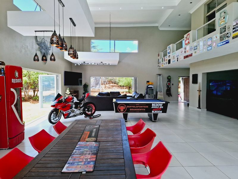 Spacious open-plan living area featuring high ceilings, tiled flooring, large bi-fold doors opening to the garden, and a mezzanine level with glass balustrades.