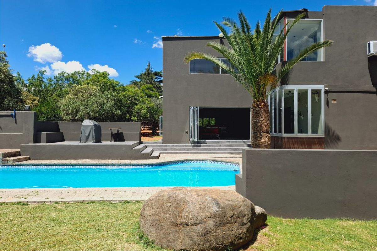 Rear exterior view featuring a swimming pool, raised patio area, and modern bi-fold doors leading into the home.