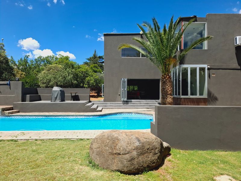 Rear exterior view featuring a swimming pool, raised patio area, and modern bi-fold doors leading into the home.