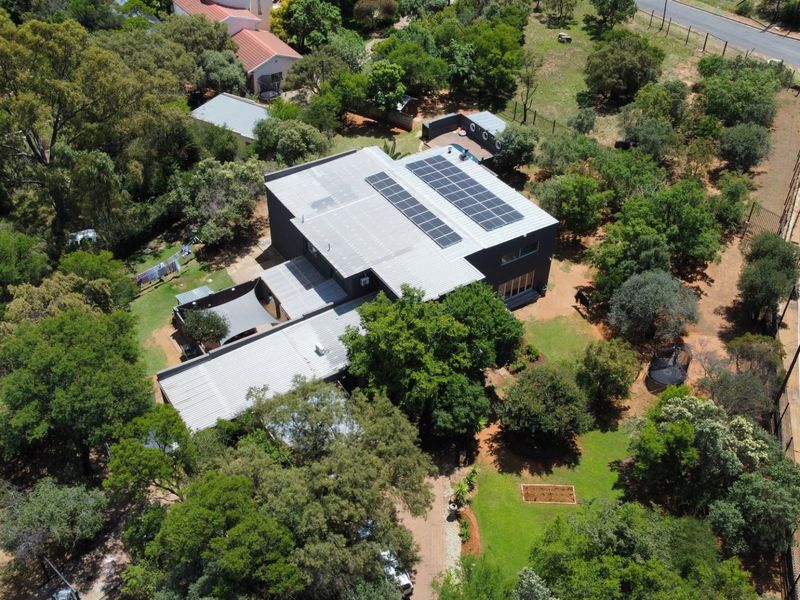 Aerial view of a modern house featuring a metal roof with integrated solar panels, set within a spacious, tree-lined property.