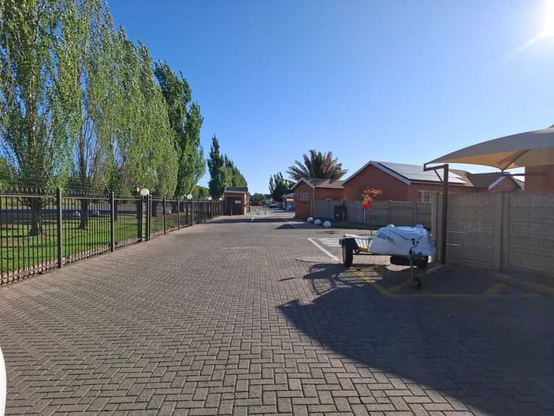 A paved driveway leading through a townhouse complex, featuring perimeter fencing, brick building facades, and a covered parking area.