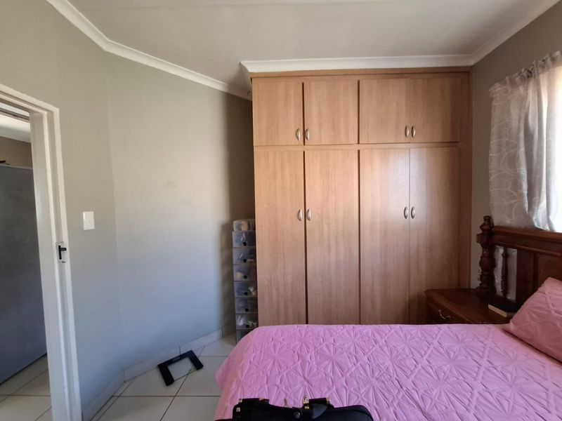 A bedroom featuring light wood-finish built-in cupboards, tiled flooring, and coved ceiling details.