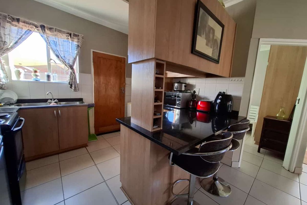A functional kitchen featuring laminate cabinetry, black granite countertops, a breakfast bar, and tiled flooring, providing a practical layout for daily meal preparation.