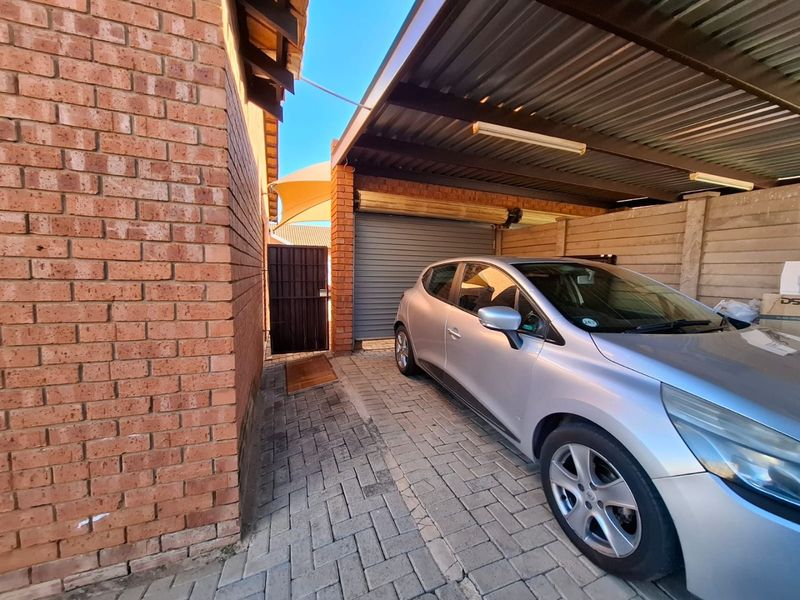 A covered carport area featuring brick walls, paved flooring, and a secure metal roller door entrance.