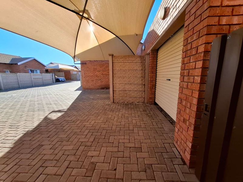A paved driveway area featuring a shade sail, face brick exterior walls, and a secure roll-up garage door.
