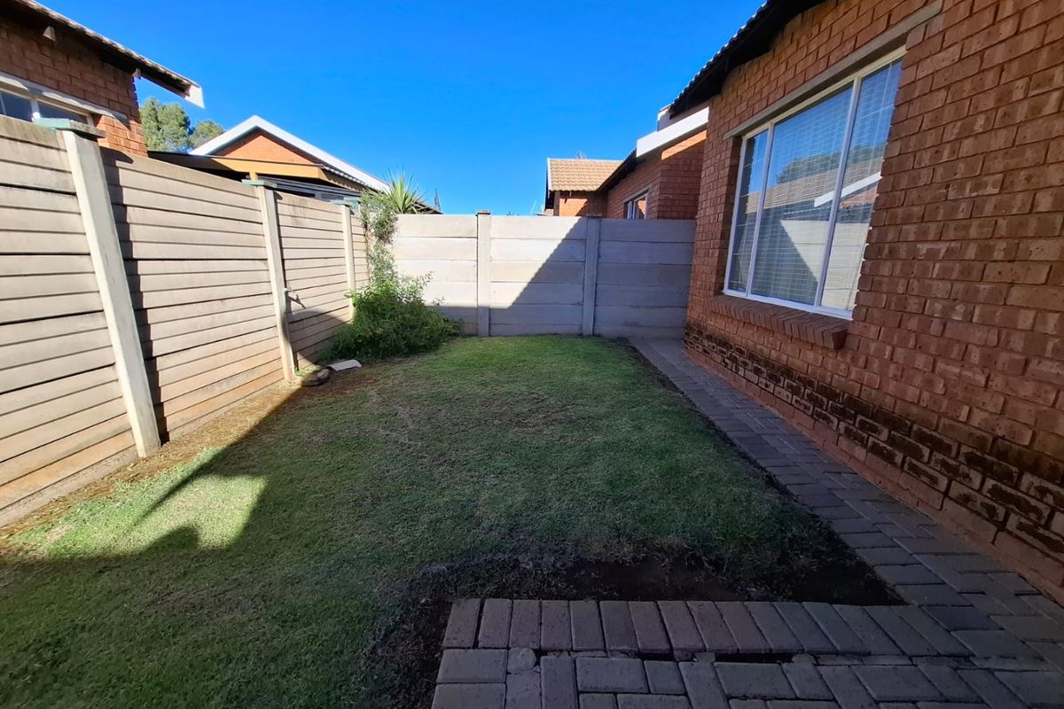 A private rear garden area featuring a small lawn, brick paved pathway, and secure precast concrete boundary walls.