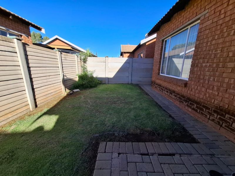 A private rear garden area featuring a small lawn, brick paved pathway, and secure precast concrete boundary walls.