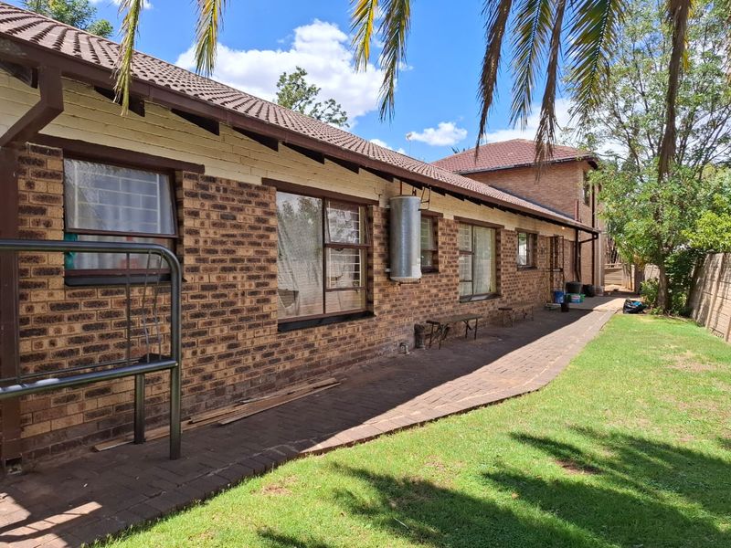 Rear view of the house featuring a brick facade, tiled roof, paved walkway, and an external geyser unit set against a garden area.