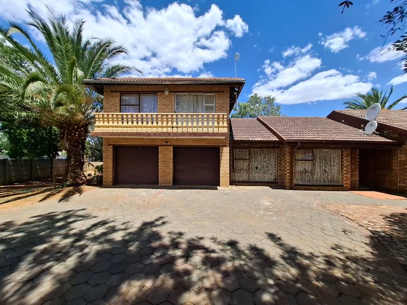 Front elevation of a double-story brick house featuring a double garage, upper-level balcony, and a paved driveway area.