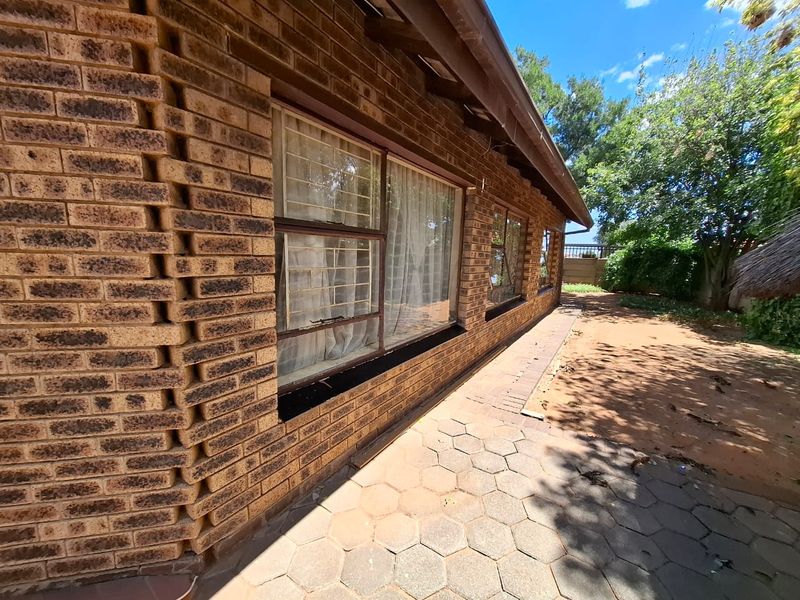 Rear exterior view of the house featuring a face brick facade, paved patio area, and security bars on the windows.