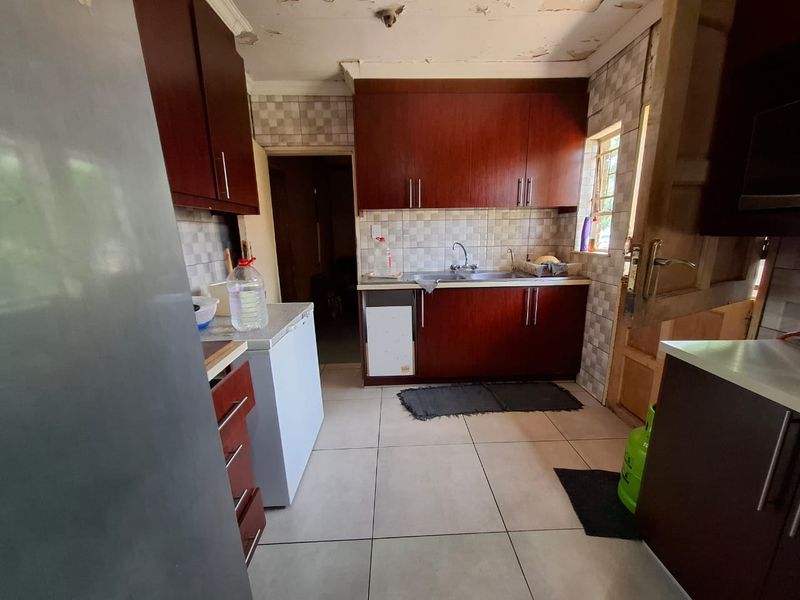 A functional kitchen featuring dark wood cabinetry, tiled backsplash, and tiled flooring, currently requiring ceiling repairs and cosmetic updates.