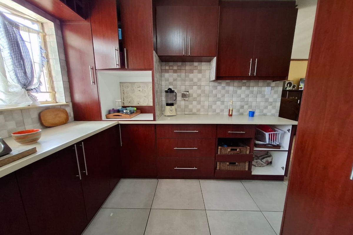 A functional kitchen featuring dark wood cabinetry, light countertops, and tiled flooring, offering ample storage space and a classic layout.