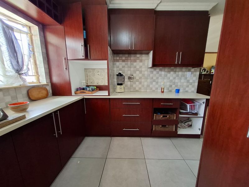 A functional kitchen featuring dark wood cabinetry, light countertops, and tiled flooring, offering ample storage space and a classic layout.
