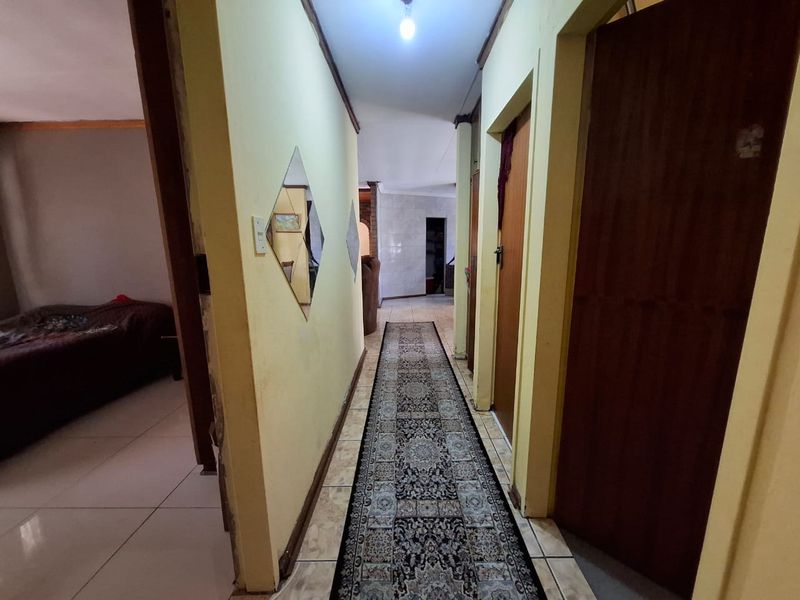 A residential hallway featuring tiled flooring and multiple wooden doors, showing signs of wear and requiring cosmetic updates.