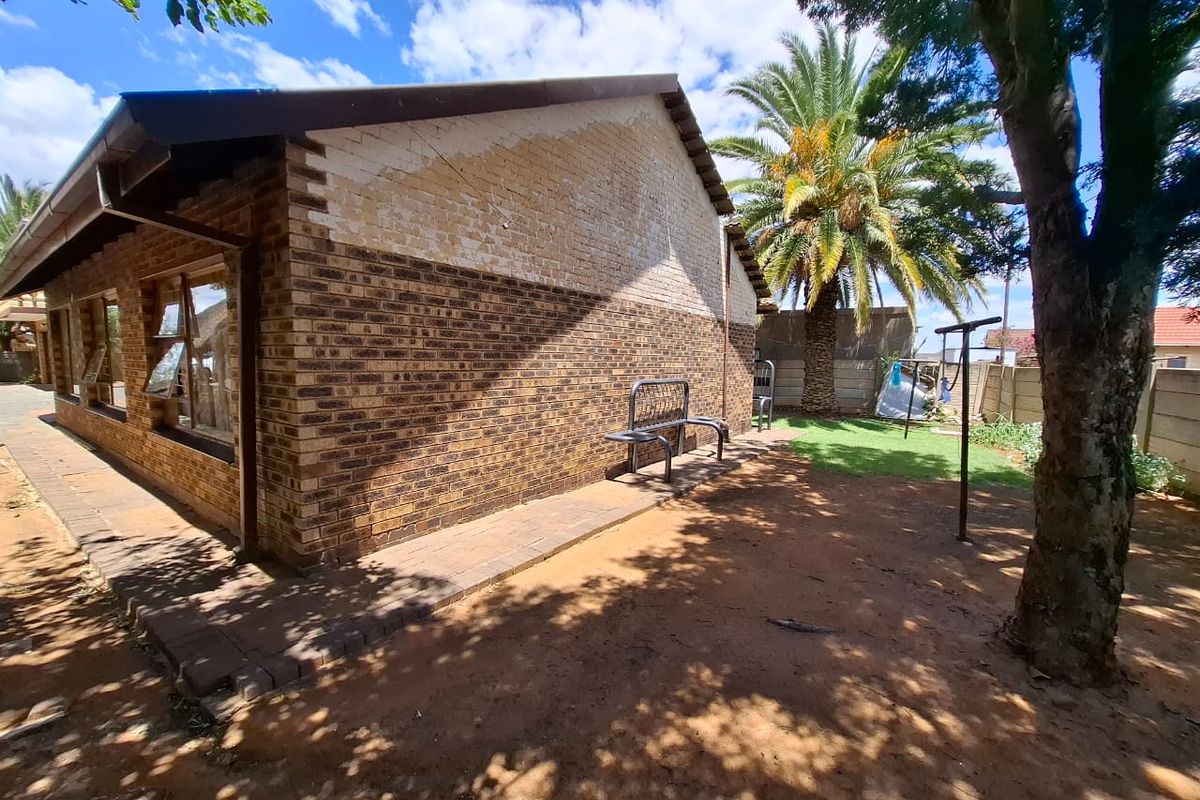 Rear exterior view of the house featuring a brick facade, paved walkway, and established garden area.