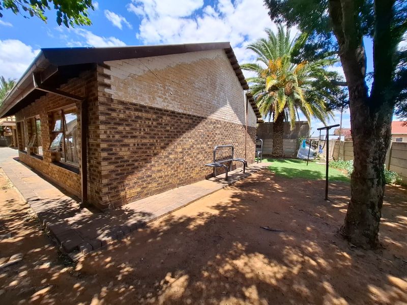 Rear exterior view of the house featuring a brick facade, paved walkway, and established garden area.