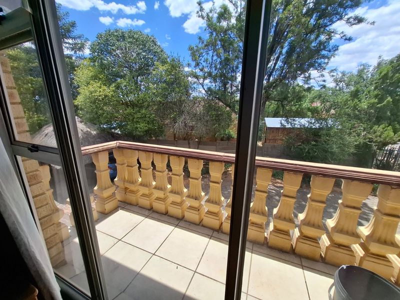 A balcony featuring a classic balustrade and tiled flooring, offering an outdoor space with views of the surrounding garden and trees.