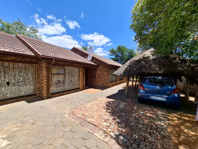 Front exterior view of a face brick house featuring a tiled roof, paved driveway, and a traditional thatched carport structure.