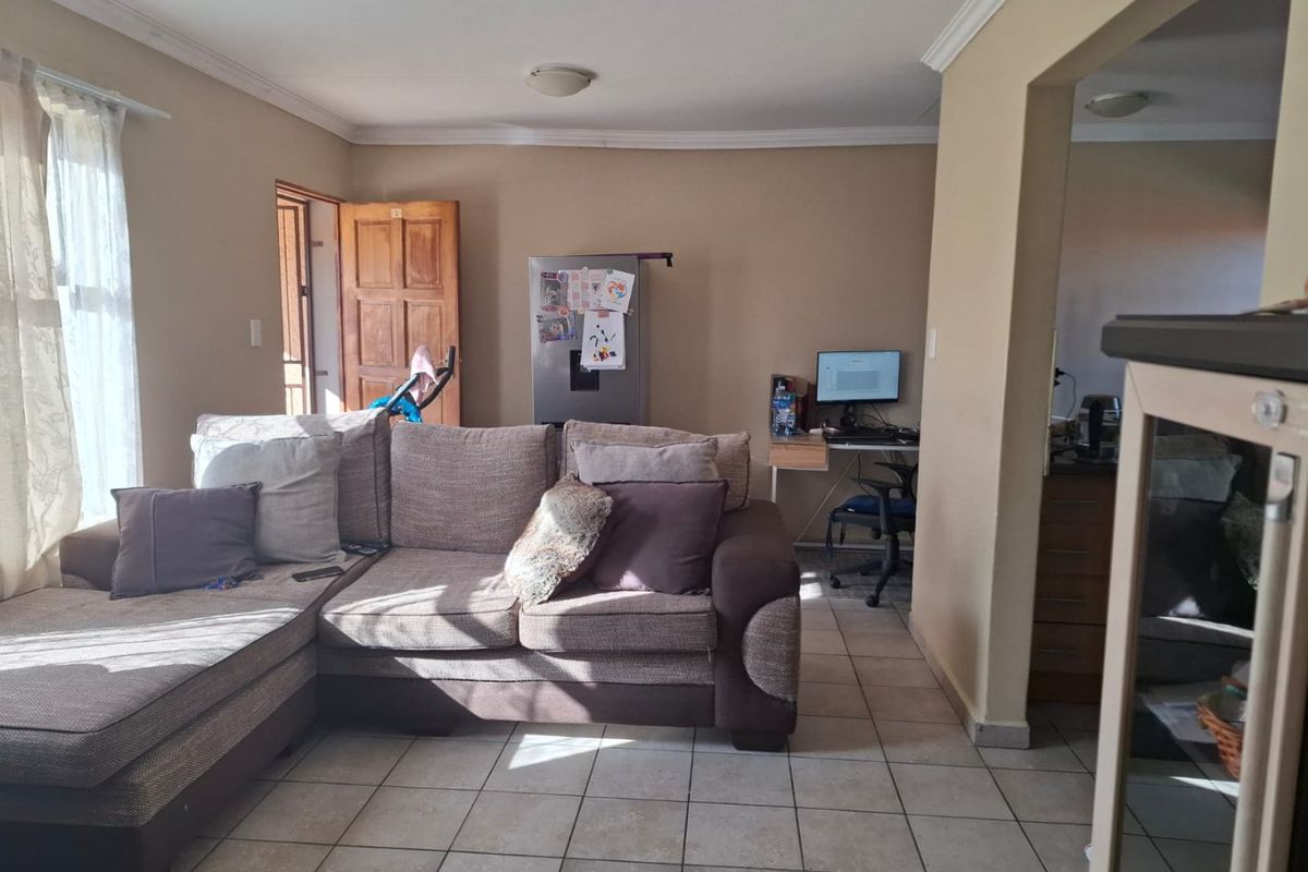 A living room area featuring tiled flooring and ceiling cornicing, providing a functional space with direct access to adjacent areas.