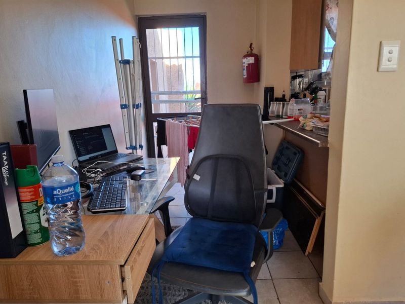 An open-plan living area featuring tiled flooring, a security gate, and integrated kitchen cabinetry, currently utilized as a multi-functional workspace.
