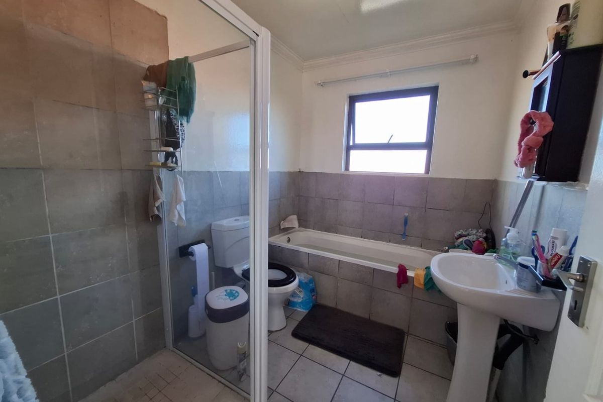 A functional bathroom featuring a pedestal basin, built-in bathtub, and a separate shower enclosure with tiled finishes throughout.