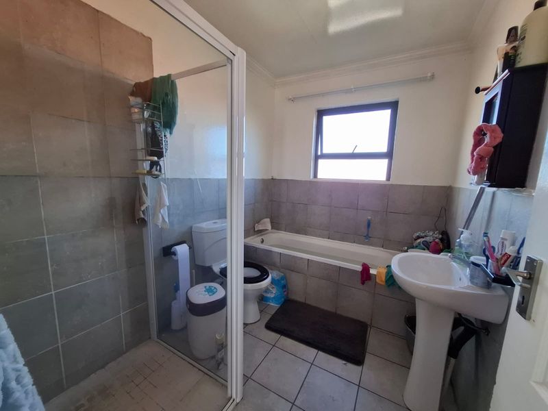 A functional bathroom featuring a pedestal basin, built-in bathtub, and a separate shower enclosure with tiled finishes throughout.