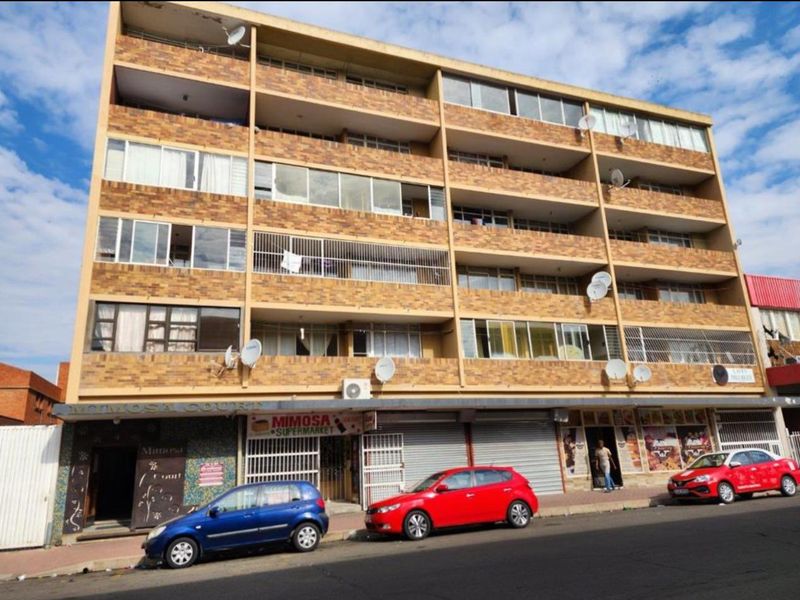 A multi-story commercial and residential building featuring a brick facade, ground-floor retail units with security shutters, and upper-level residential balconies.
