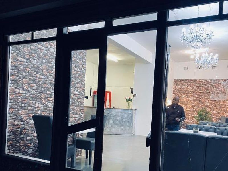 Open-plan commercial space featuring a stone-effect accent wall, metal service counter, and large glass storefront entrance with visible structural damage to the glass.