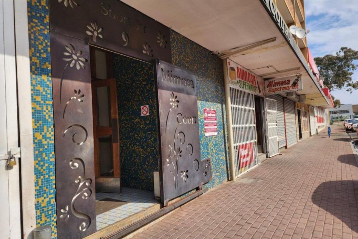 Street-level view of a commercial building entrance featuring decorative metal security gates and mosaic tile detailing along the storefront facade.