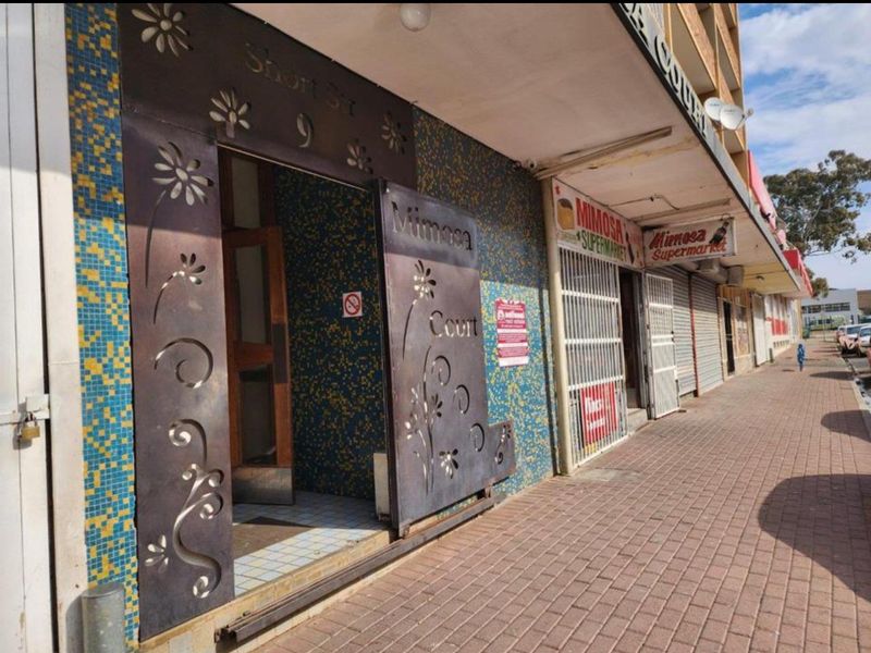 Street-level view of a commercial building entrance featuring decorative metal security gates and mosaic tile detailing along the storefront facade.