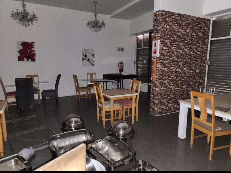 Open plan commercial dining area featuring a stone-effect feature wall, tiled flooring, and integrated security shutters.