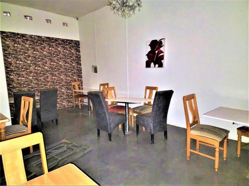 Open plan commercial dining area featuring a stone-effect accent wall, concrete flooring, and decorative lighting, suitable for a cafe or restaurant setting.