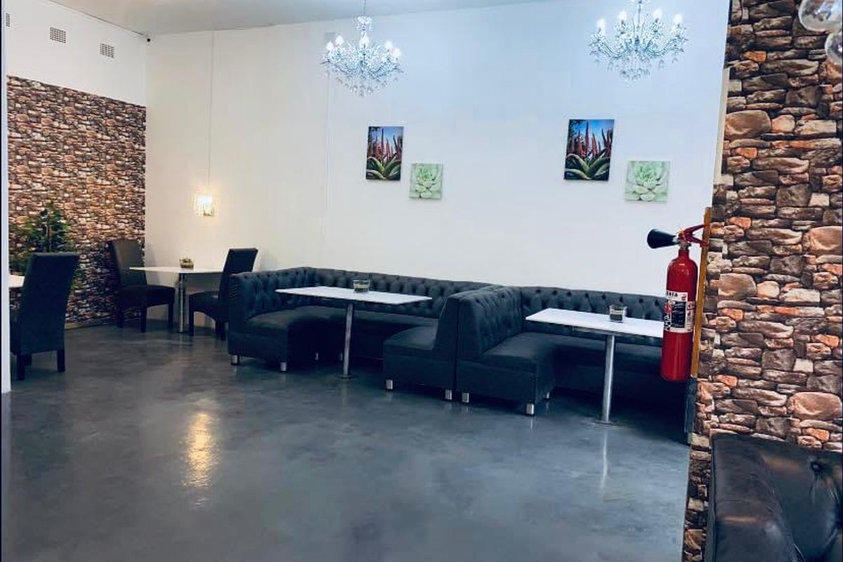 Commercial interior space featuring polished concrete floors, stone veneer accent walls, and elegant crystal chandeliers, suitable for a restaurant or lounge setting.