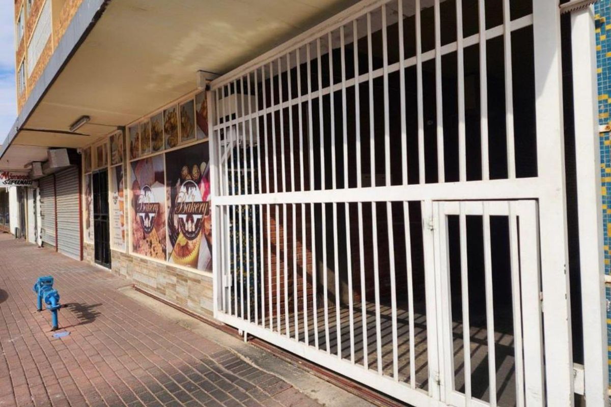 Commercial storefront featuring a secure metal gate, brick facade, and paved walkway access.