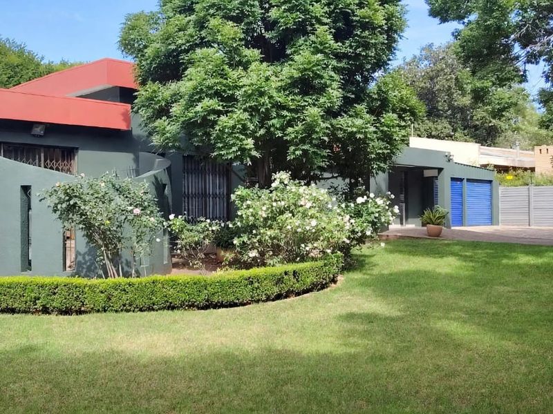 Rear view of the property featuring a spacious lawn, paved driveway, garage access, and established garden landscaping.
