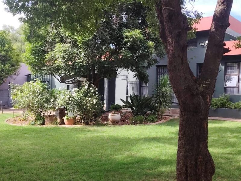 A well-maintained rear garden featuring a lush lawn, established trees, and a brick-edged garden bed set against the rear facade of the house.