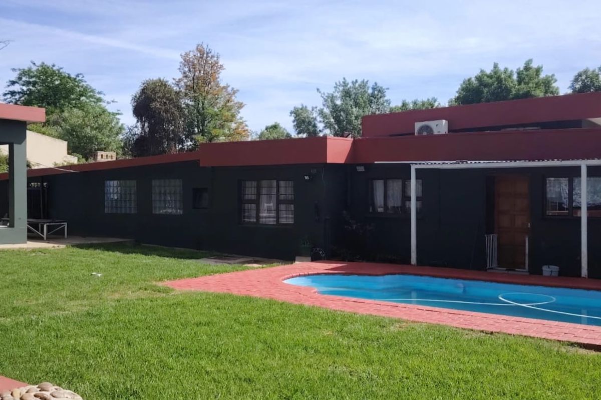 Rear exterior view of the house featuring a swimming pool, paved patio area, and a well-maintained lawn.