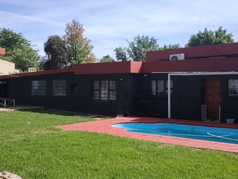 Rear exterior view of the house featuring a swimming pool, paved patio area, and a well-maintained lawn.