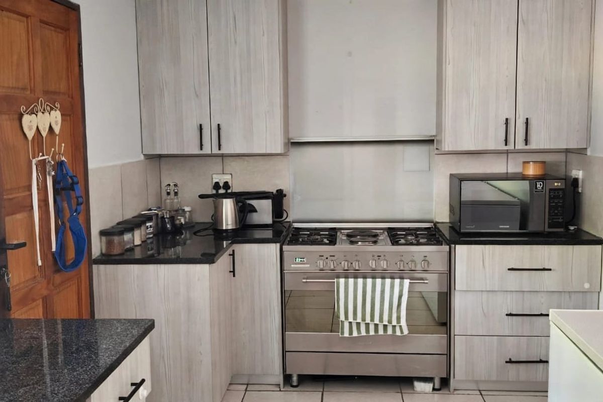 A functional kitchen featuring light wood-grain cabinetry, dark granite countertops, a gas stove with extractor fan, and neutral tiled flooring.